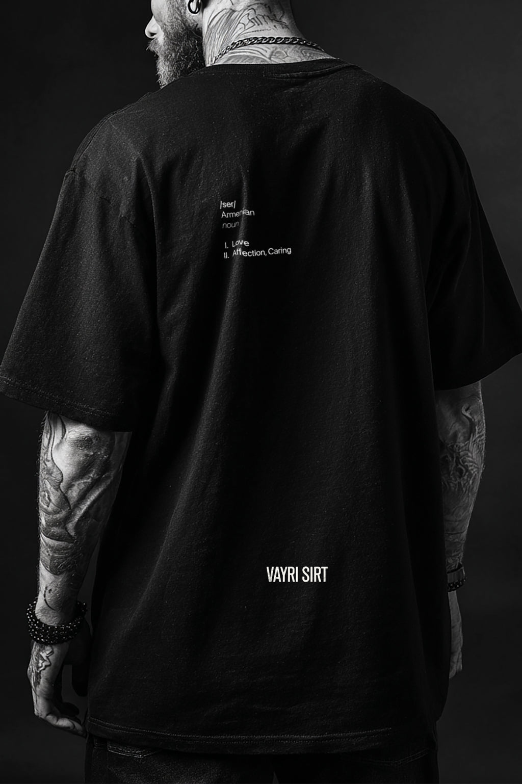 Person wearing a black t-shirt with text on the back, standing against a dark background