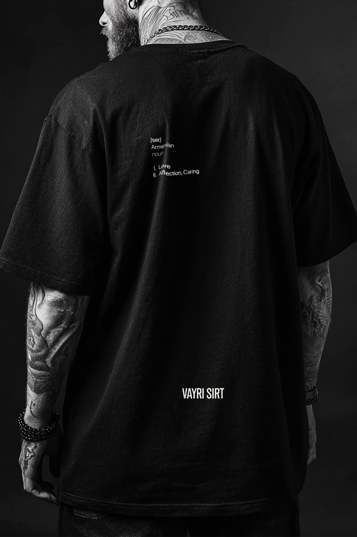 Person wearing a black t-shirt with text on the back, standing against a dark background