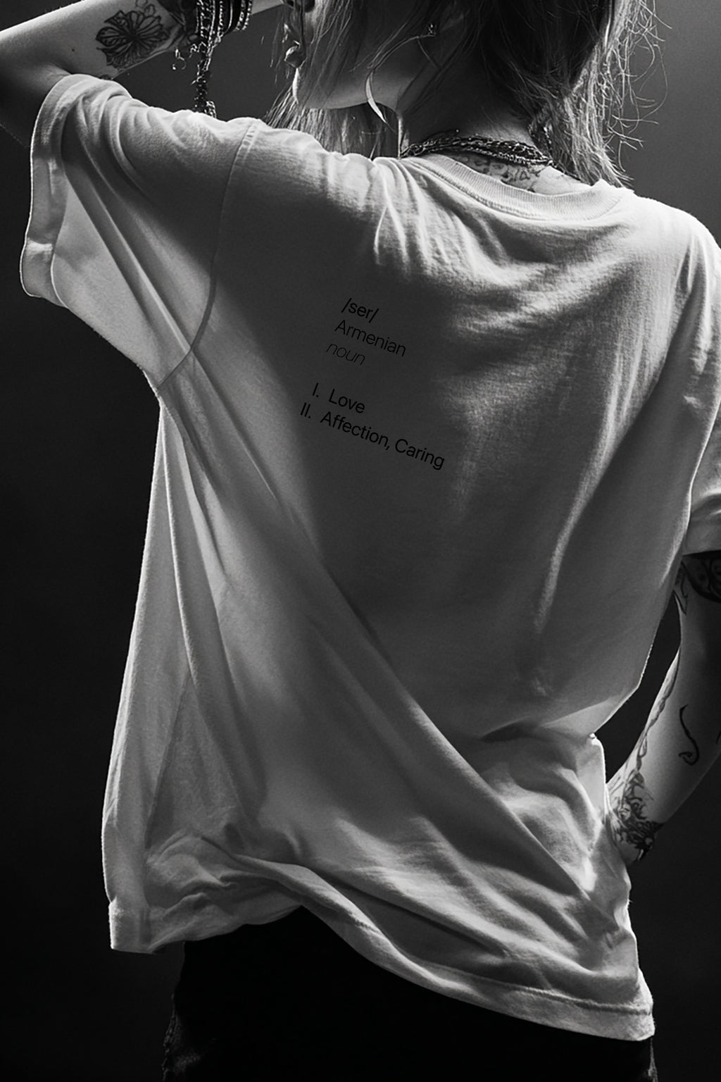 Person wearing a white t-shirt with text on the back, standing against a dark background