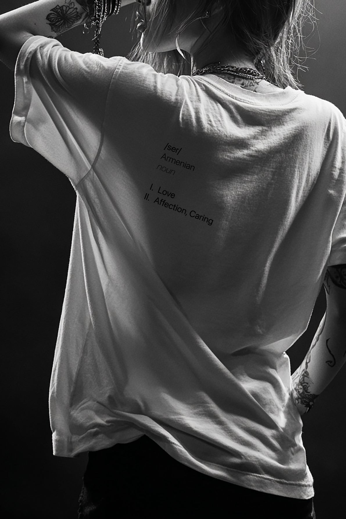 Person wearing a white t-shirt with text on the back, standing against a dark background